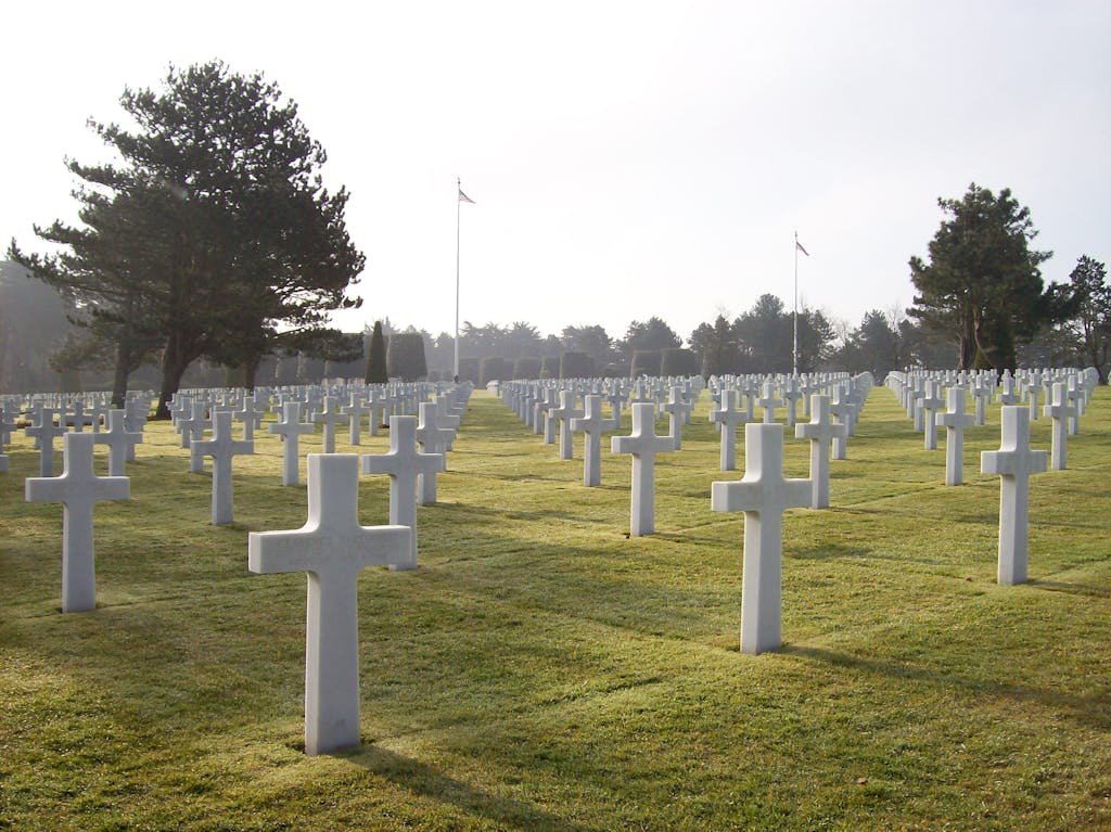A serene military cemetery with rows of white crosses under sunlight, symbolizing remembrance.