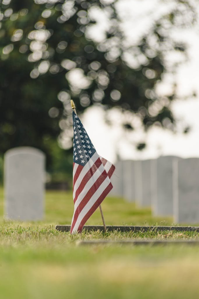 American flag stands among tombstones in a serene cemetery with a blurred background, representing national remembrance.
