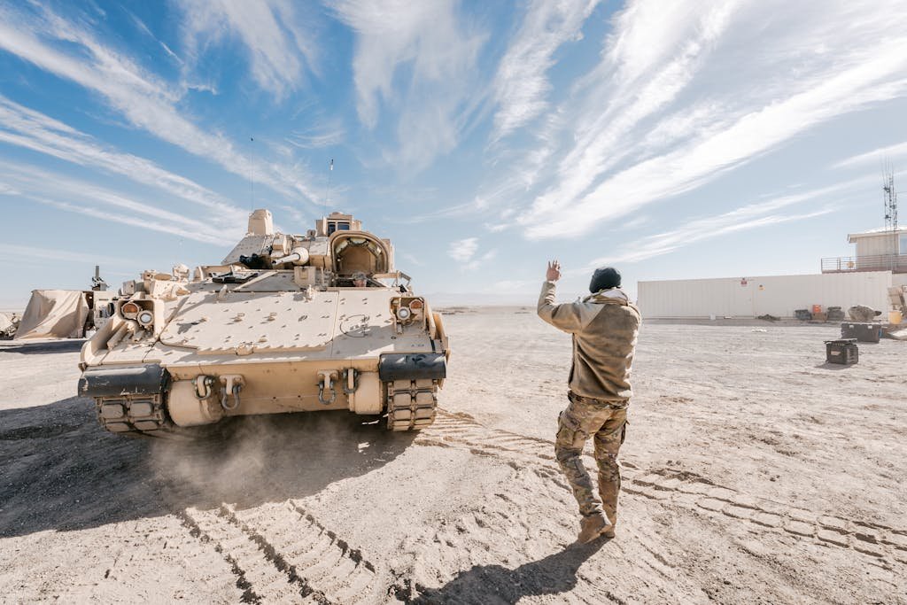 Bradley Fighting Vehicle and soldier in desert training operation under clear sky.