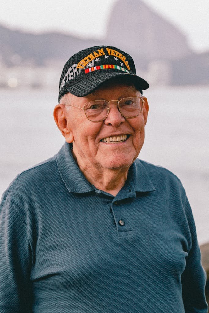 Elderly man wearing a Vietnam veteran cap, smiling near the ocean.