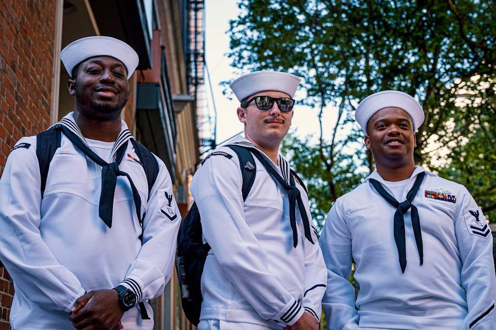 Three navy sailors pose outdoors in uniform, showcasing diversity and camaraderie.